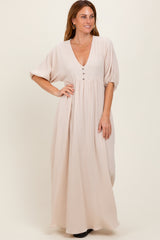 woman wearing a light beige maxi dress with a deep v-neck and button details, standing with hands on hips