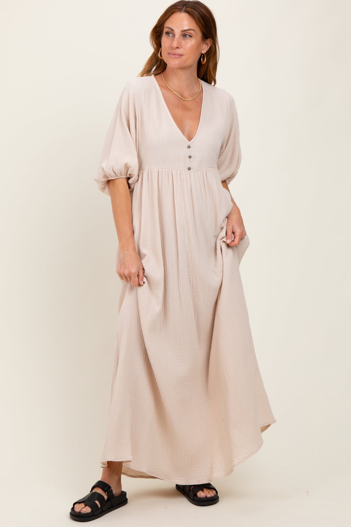 woman wearing a beige maxi dress with a v-neckline and puff sleeves, standing casually