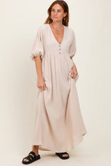 woman wearing a beige maxi dress with a v-neckline and puff sleeves, standing casually