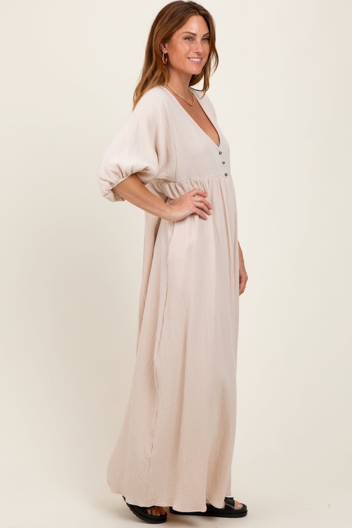woman wearing a beige maxi dress with a deep v-neck and button detail, featuring loose sleeves and a flowy silhouette