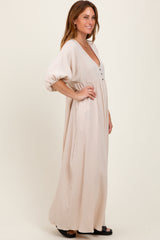 woman wearing a beige maxi dress with a deep v-neck and button detail, featuring loose sleeves and a flowy silhouette