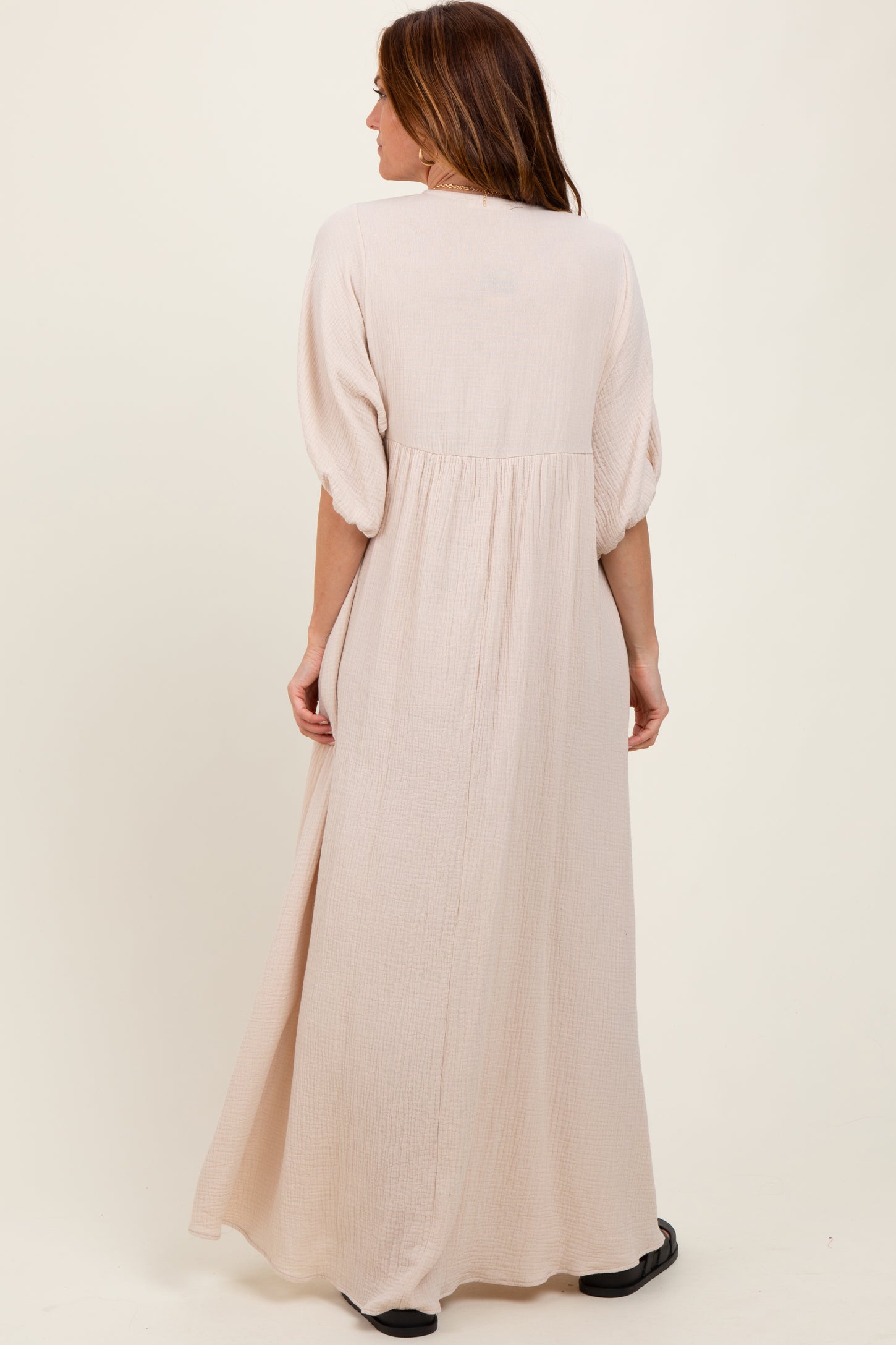 woman wearing a long beige maxi dress with puff sleeves and a gathered back detail