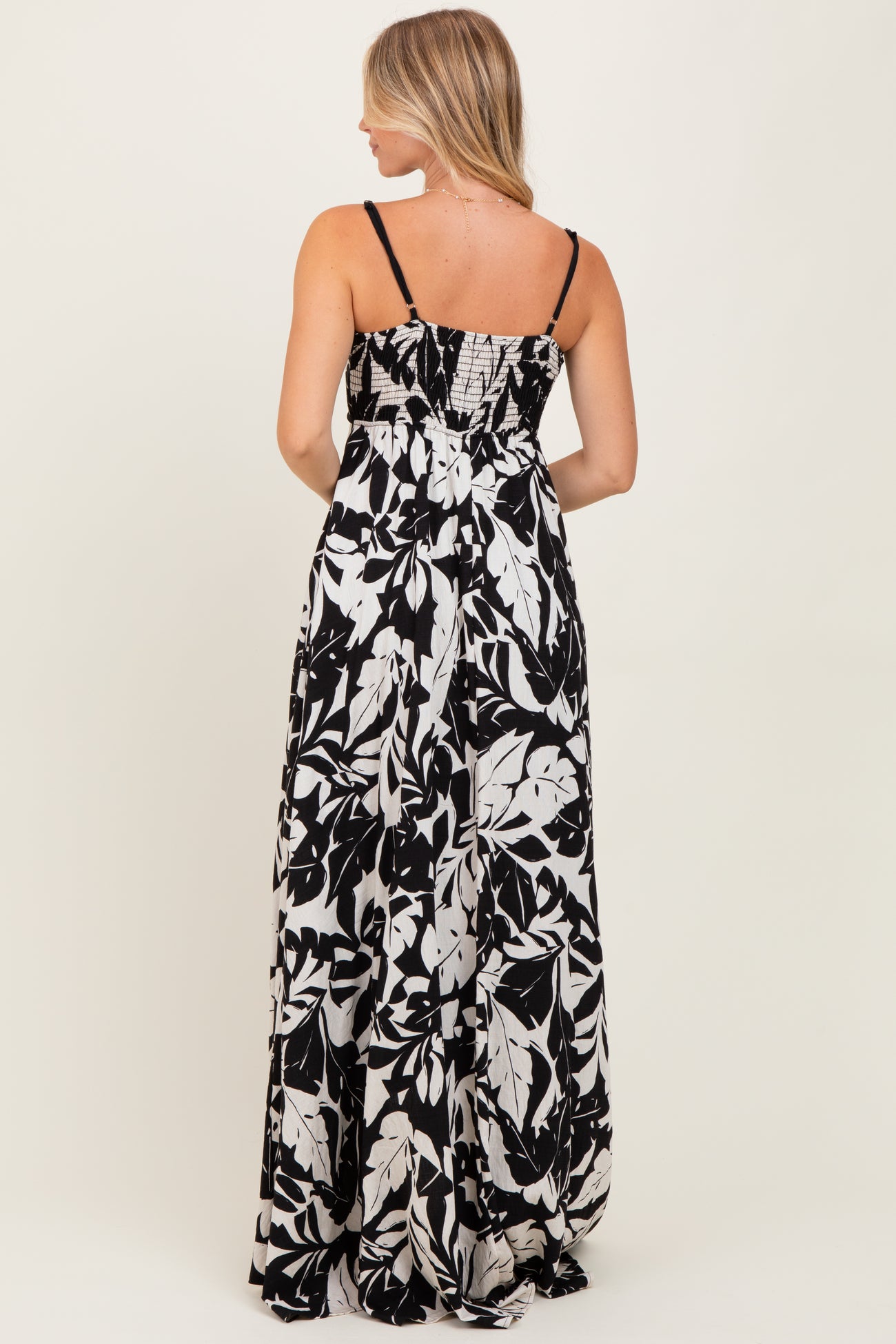 woman standing in a back view of a black and white floral maxi dress with spaghetti straps and a smocked bodice