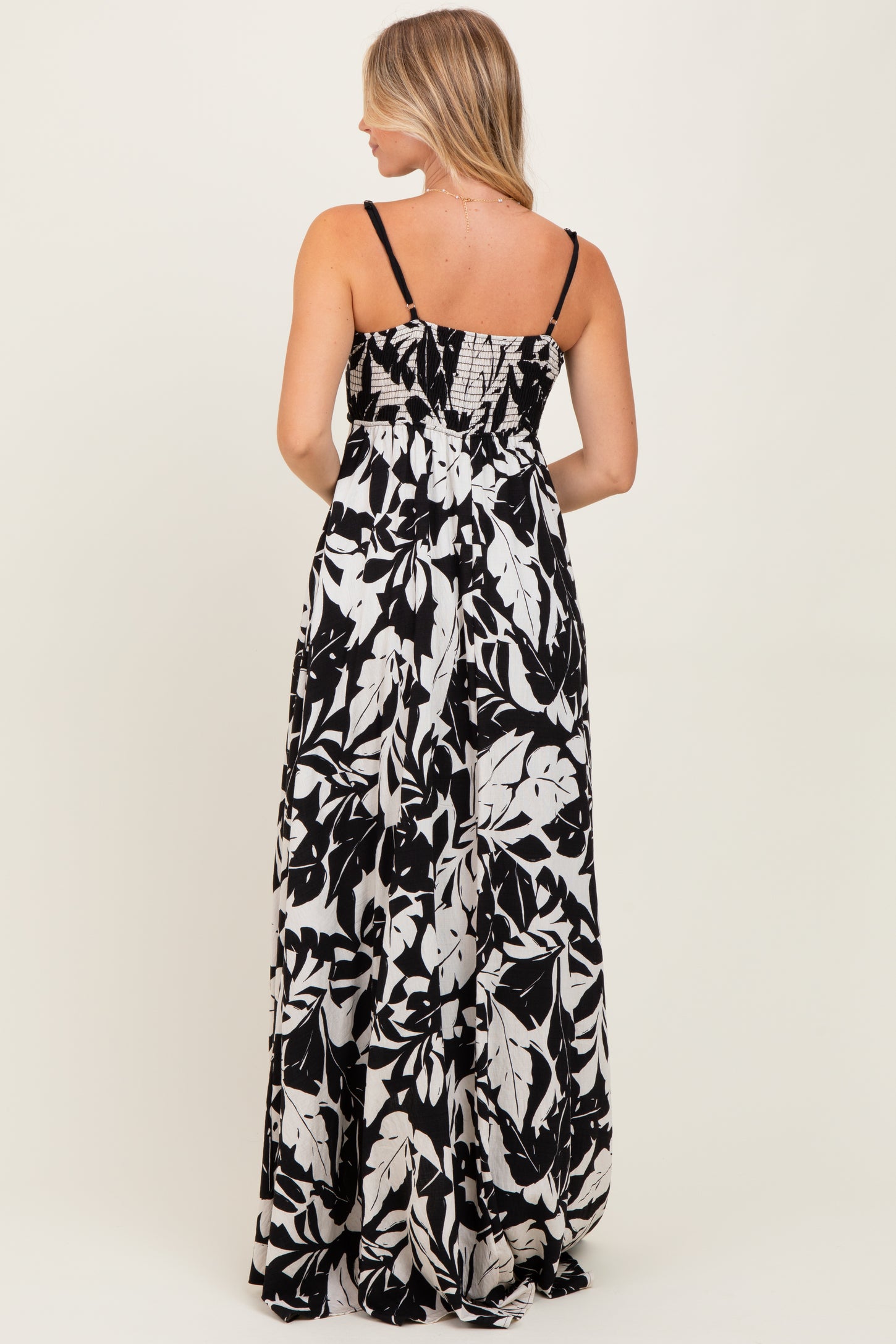 woman standing in a back view of a black and white floral maxi dress with spaghetti straps and a smocked bodice