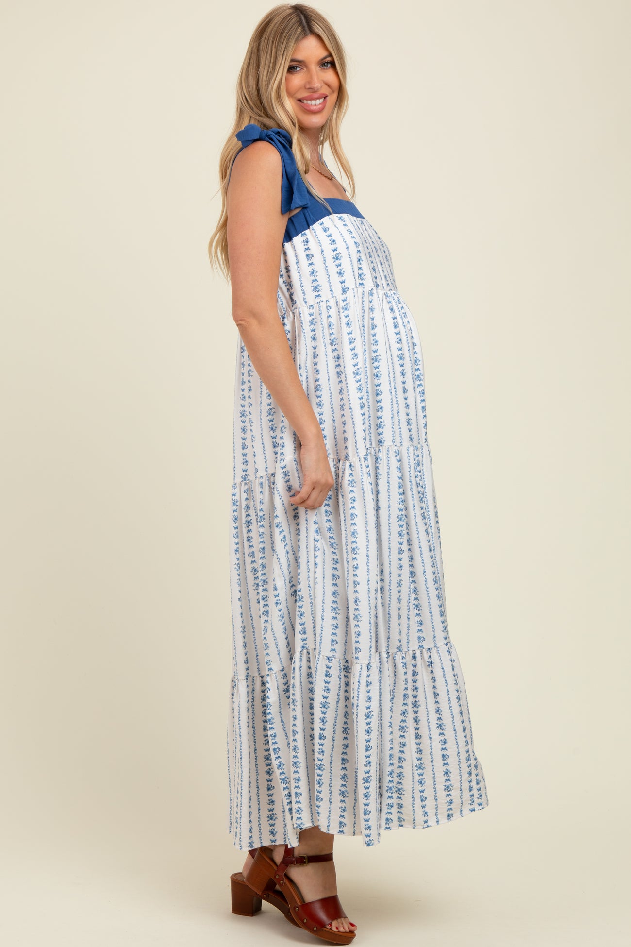 woman wearing a white and blue floral print maternity maxi dress with ruffle straps and a visible baby bump