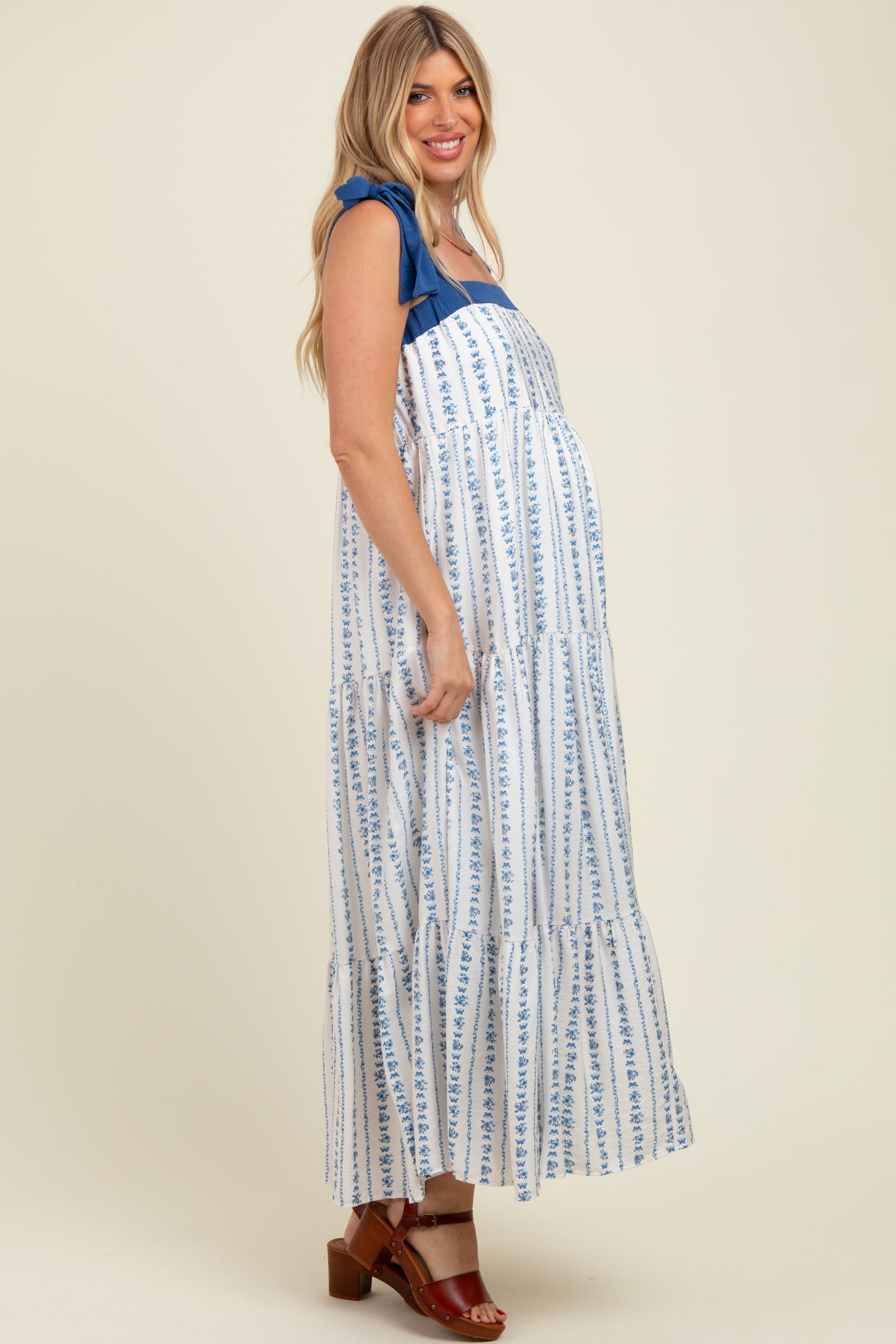 woman wearing a white and blue floral print maternity maxi dress with ruffle straps and a visible baby bump