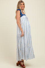 woman wearing a white and blue floral print maternity maxi dress with ruffle straps and a visible baby bump