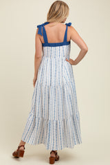 woman wearing a blue and white floral maternity dress with tiered layers and bow straps, showing her baby bump