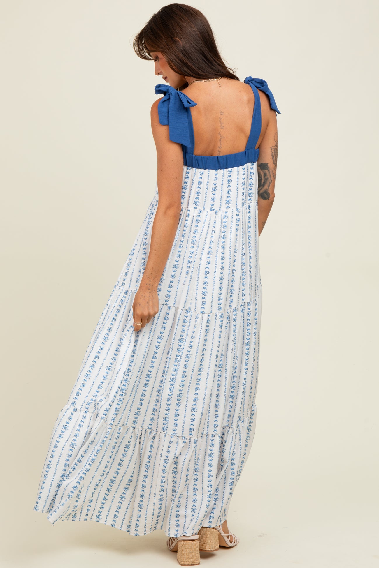 woman wearing a white maxi dress with blue stripes and bow shoulder straps, showing a tiered design from the back