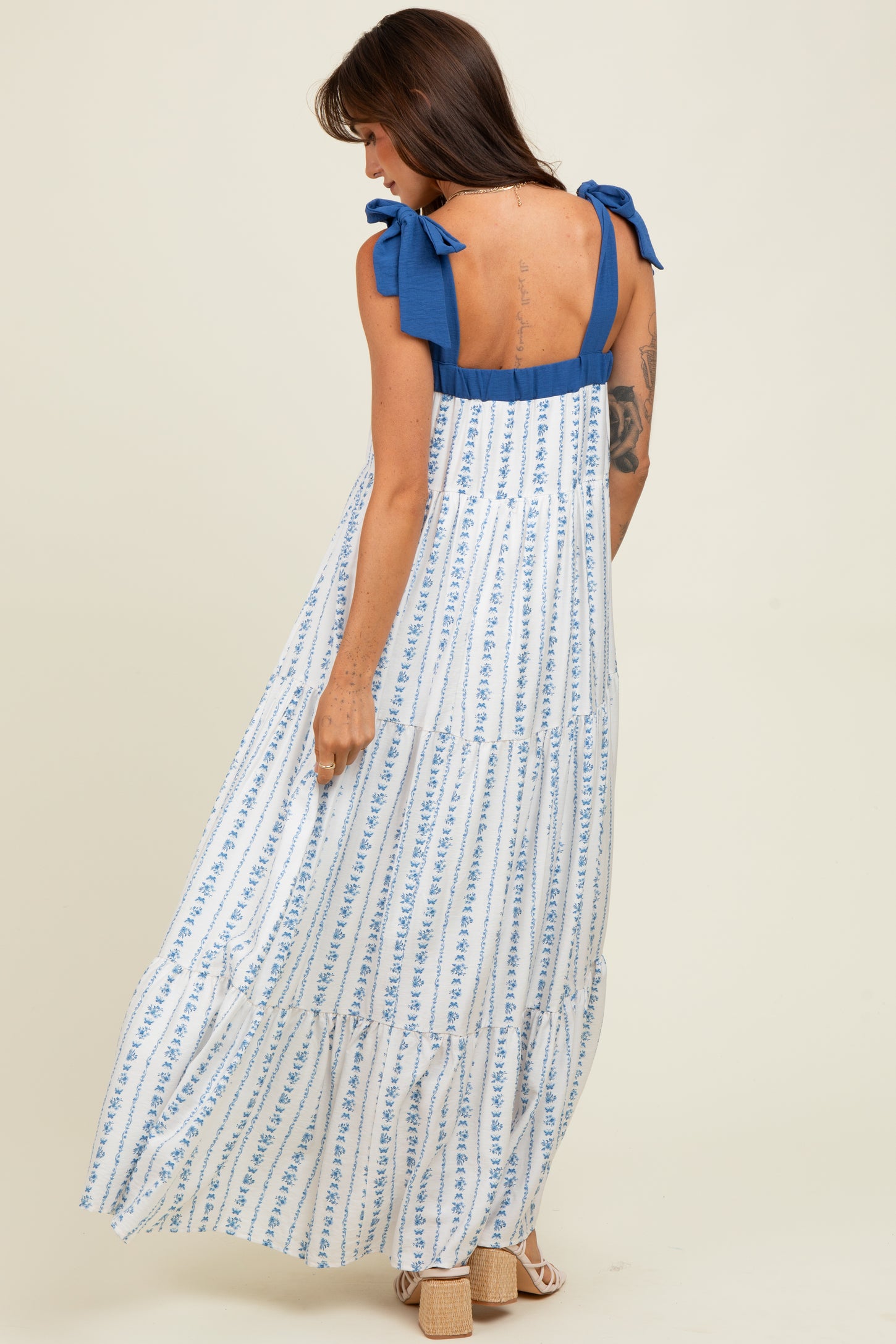 woman wearing a white maxi dress with blue stripes and bow shoulder straps, showing a tiered design from the back