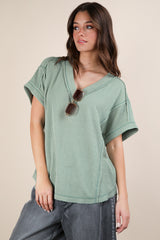 woman wearing a green short sleeve v-neck top with textured fabric and relaxed fit, paired with gray high-waisted pants