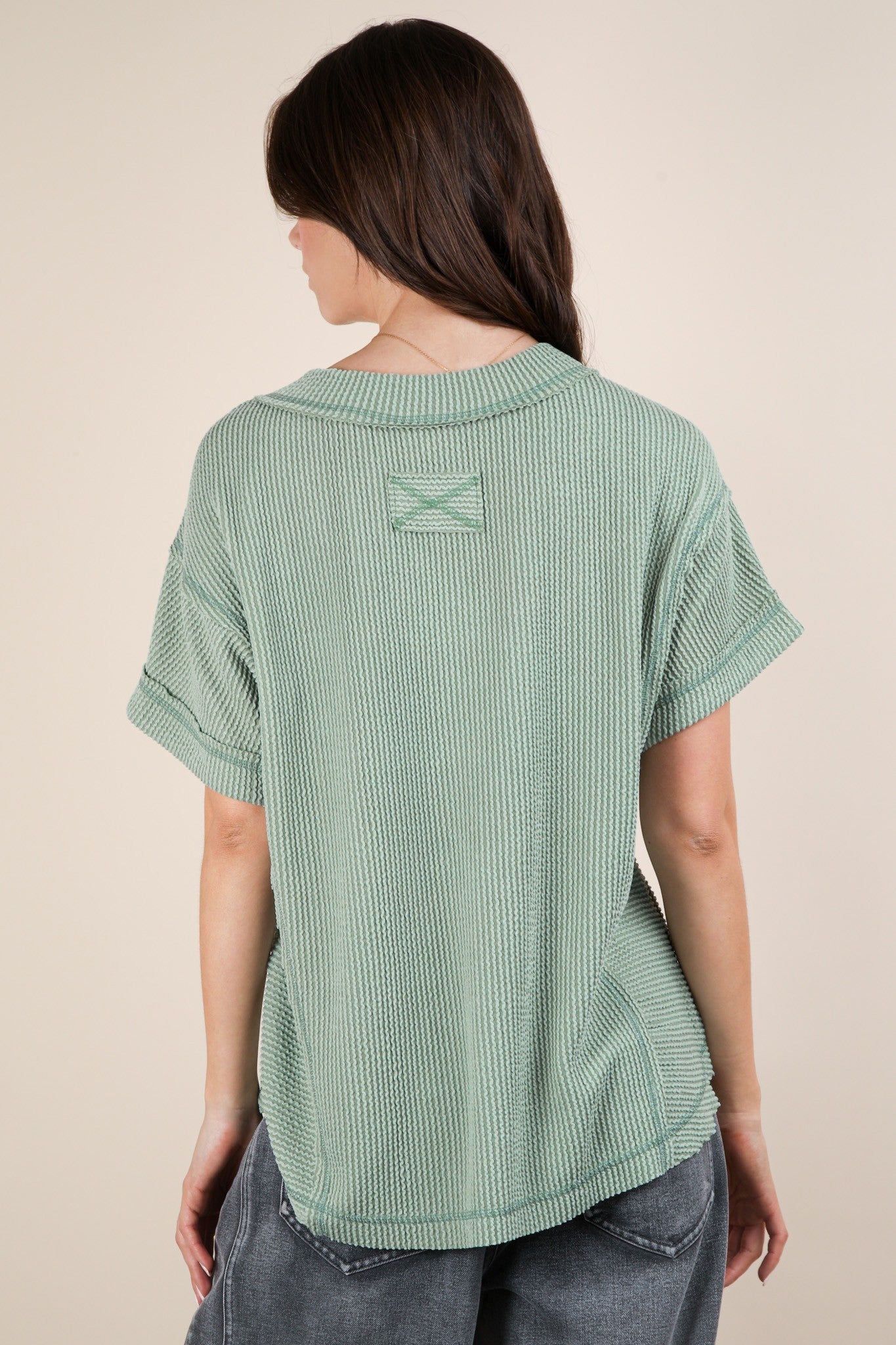 woman wearing a light green short sleeve textured top, seen from the back, styled with rolled sleeves
