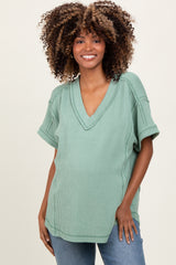 woman wearing a green v-neck maternity top with short sleeves and a visible baby bump