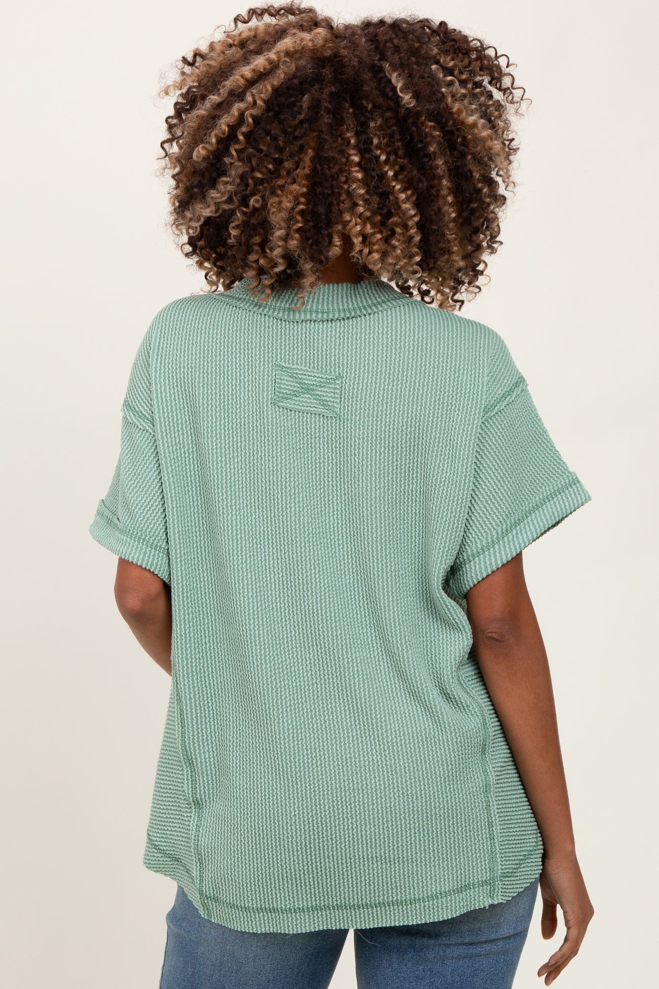 woman wearing a sage green short sleeve maternity top viewed from the back, featuring a relaxed fit and rolled sleeves