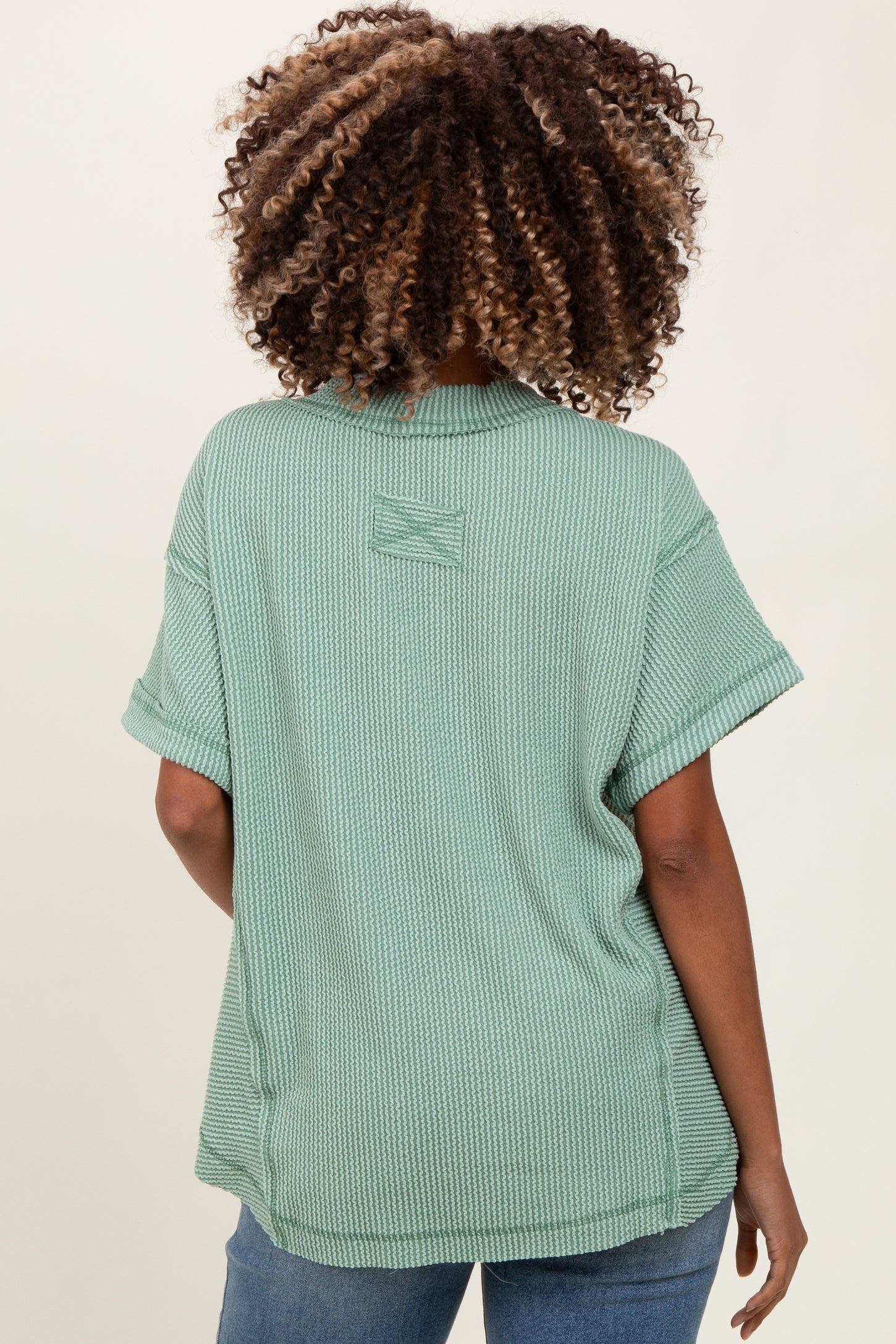 woman wearing a sage green short sleeve maternity top viewed from the back, featuring a relaxed fit and rolled sleeves