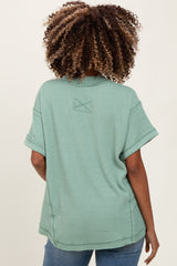 woman wearing a sage green short sleeve maternity top viewed from the back, featuring a relaxed fit and rolled sleeves