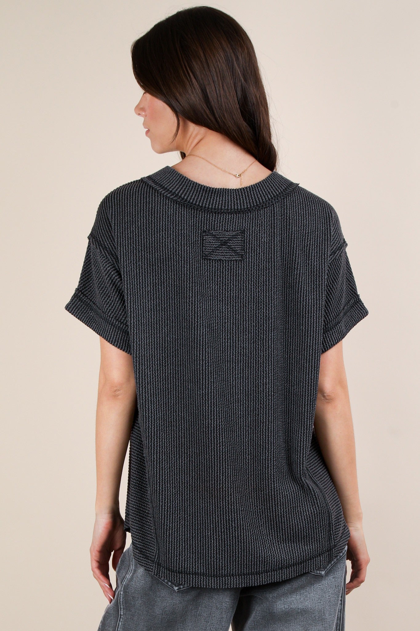 woman wearing a dark gray oversized short sleeve top with a textured knit design, showing the back view