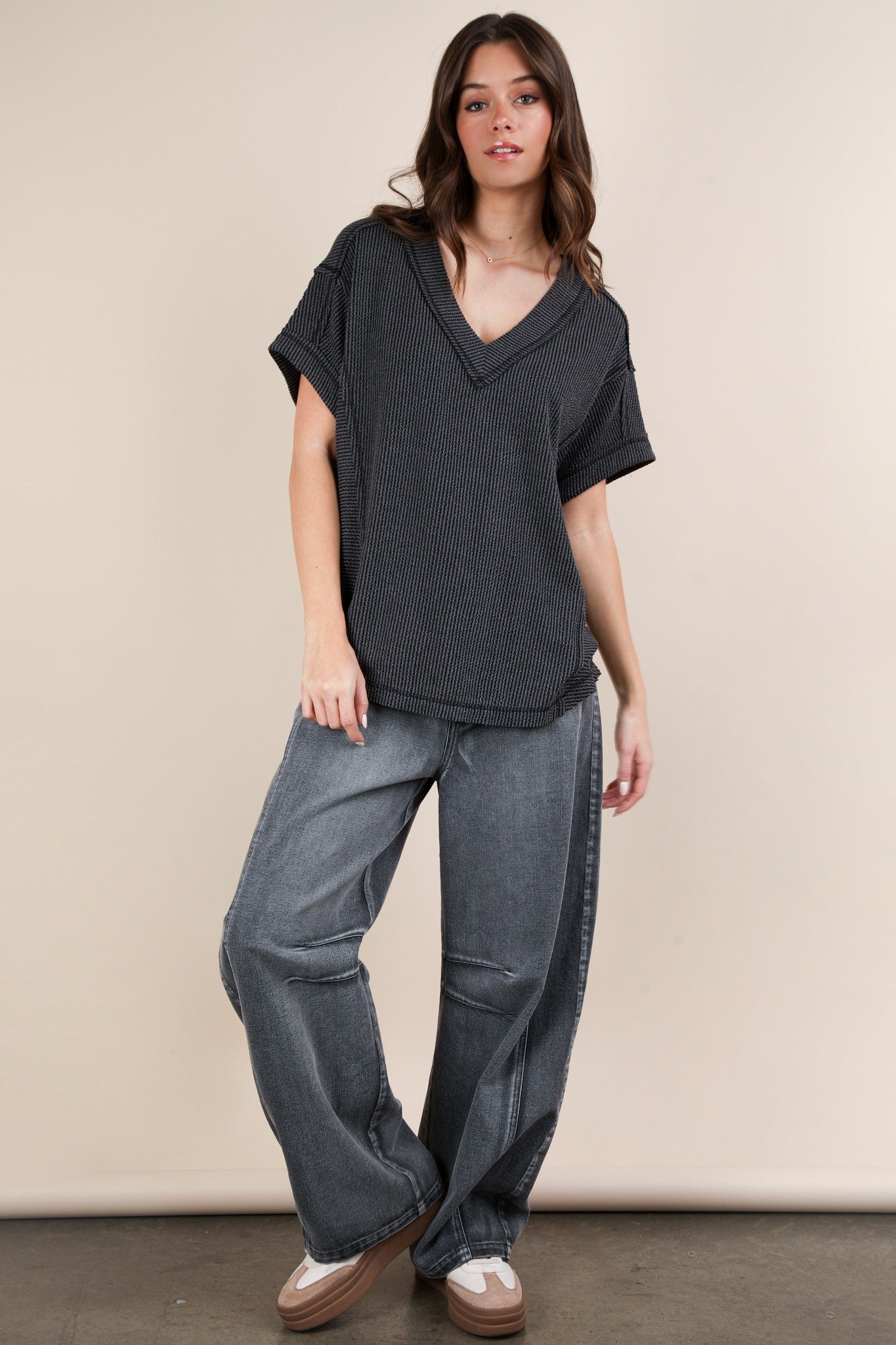 woman wearing a black striped v-neck oversized top and gray wide-leg jeans, standing against a neutral background