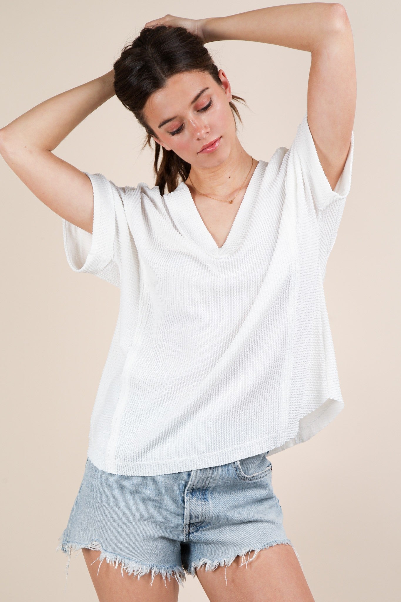 woman wearing a white short sleeve v-neck sweater with a relaxed fit paired with distressed denim shorts