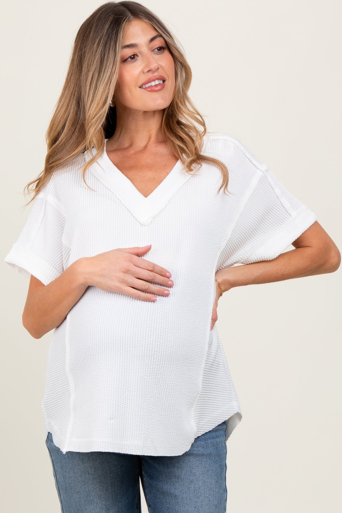 woman wearing a white short sleeve v-neck maternity top and gently holding her baby bump