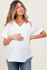 woman wearing a white short sleeve v-neck maternity top and gently holding her baby bump