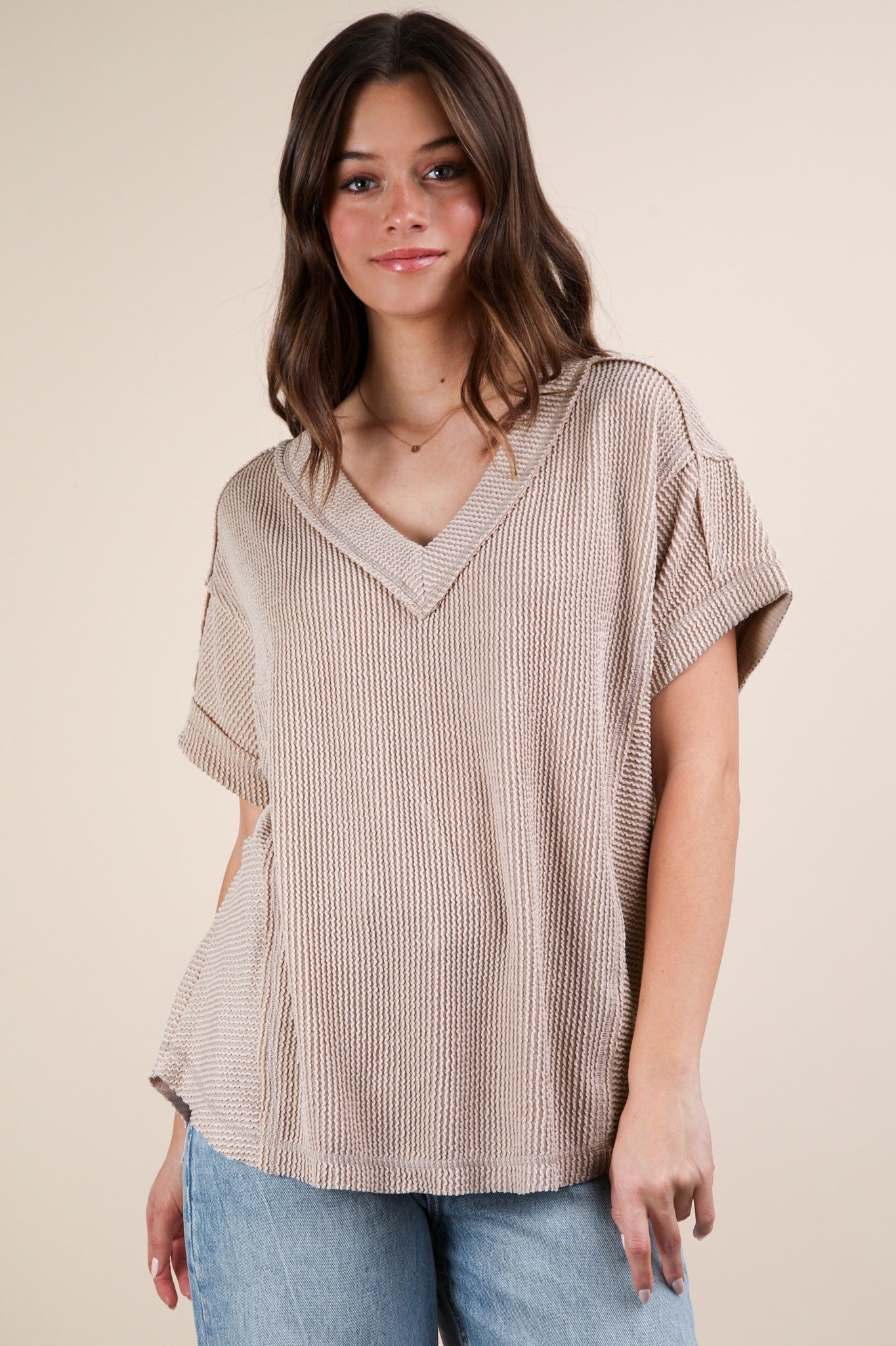 woman wearing a beige oversized v-neck knit top with short sleeves and a relaxed fit