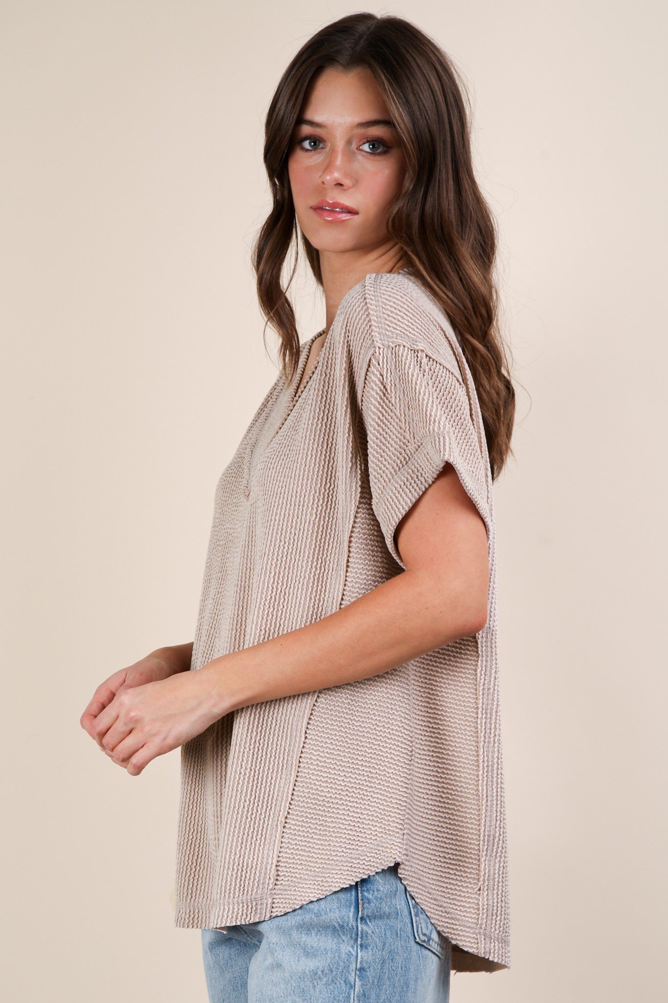 woman wearing a beige short sleeve knit top with a relaxed fit and side slits, paired with light blue jeans