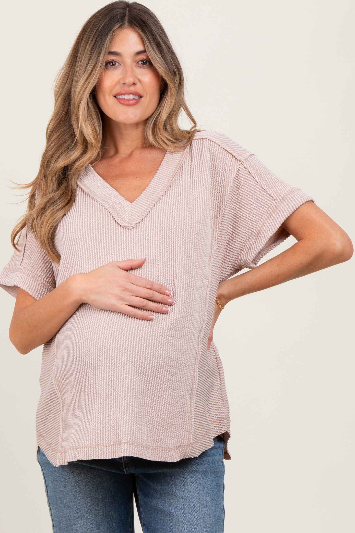 woman wearing a light pink maternity ribbed short sleeve top and holding her baby bump