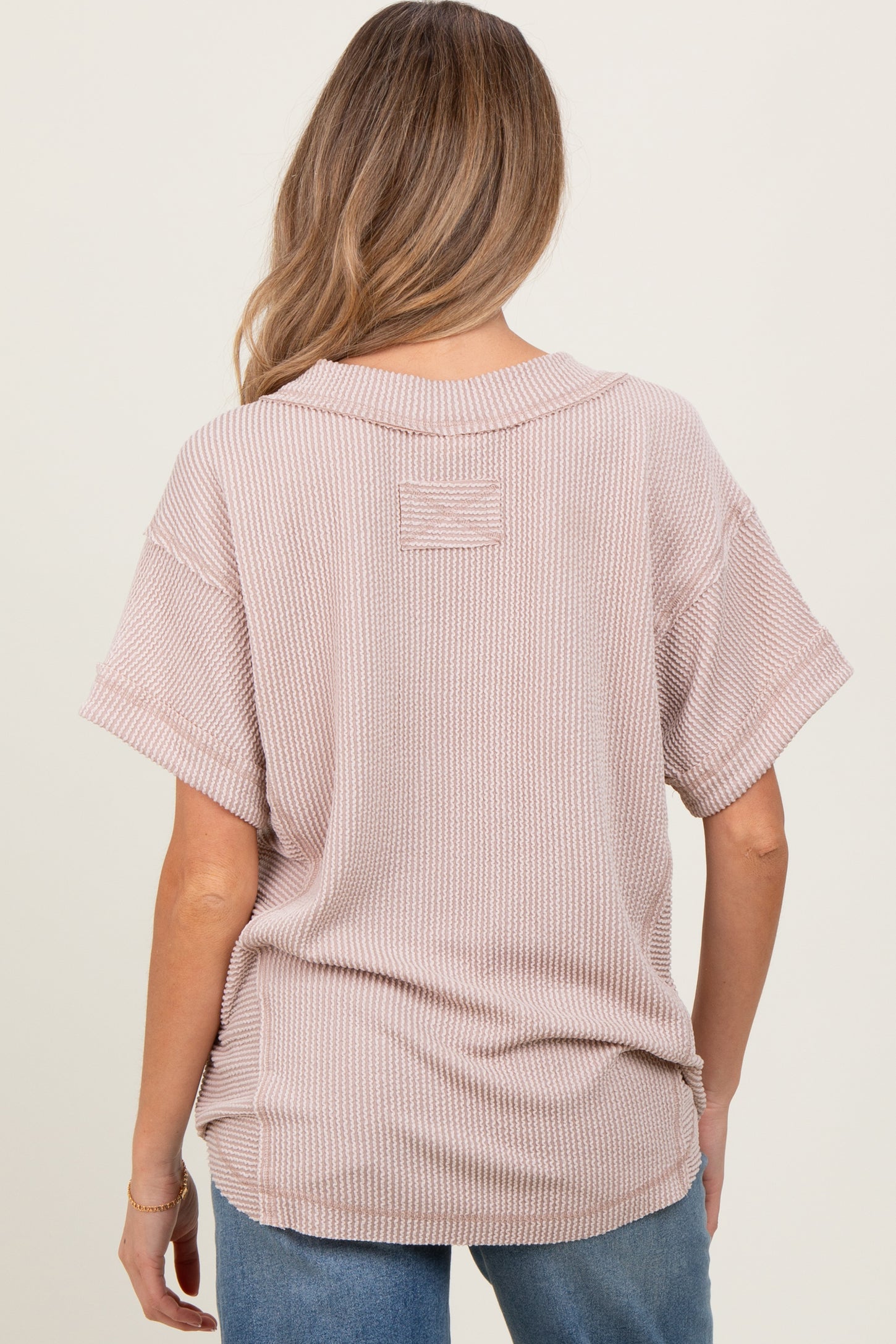 woman wearing a light pink oversized maternity top with a textured pattern, seen from the back