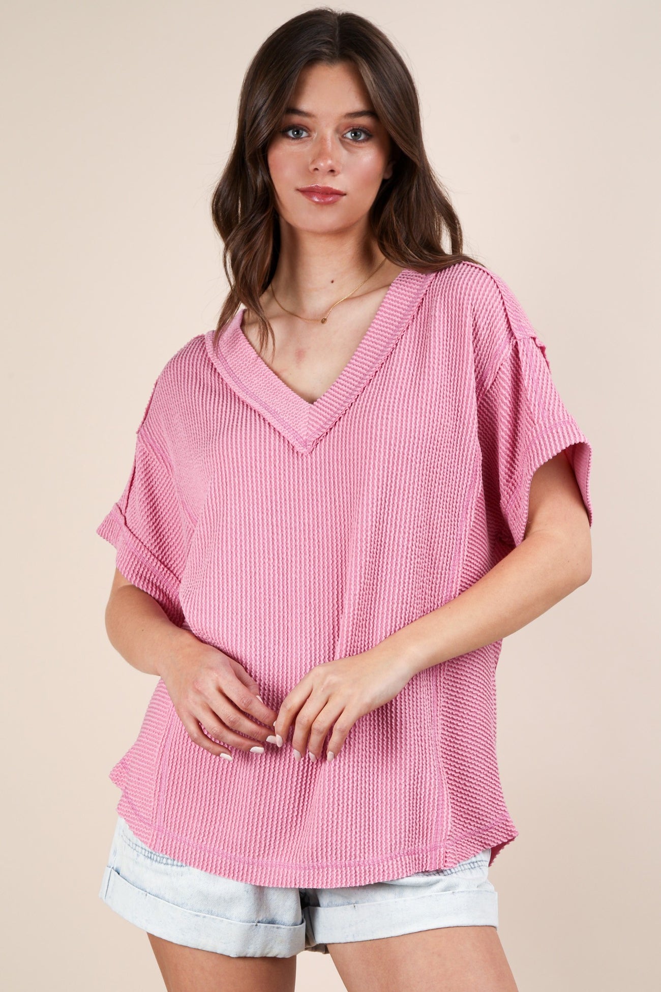 woman wearing a loose-fitting pink v-neck knit top with short sleeves and distressed denim shorts