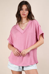woman wearing a loose-fitting pink v-neck knit top with short sleeves and distressed denim shorts