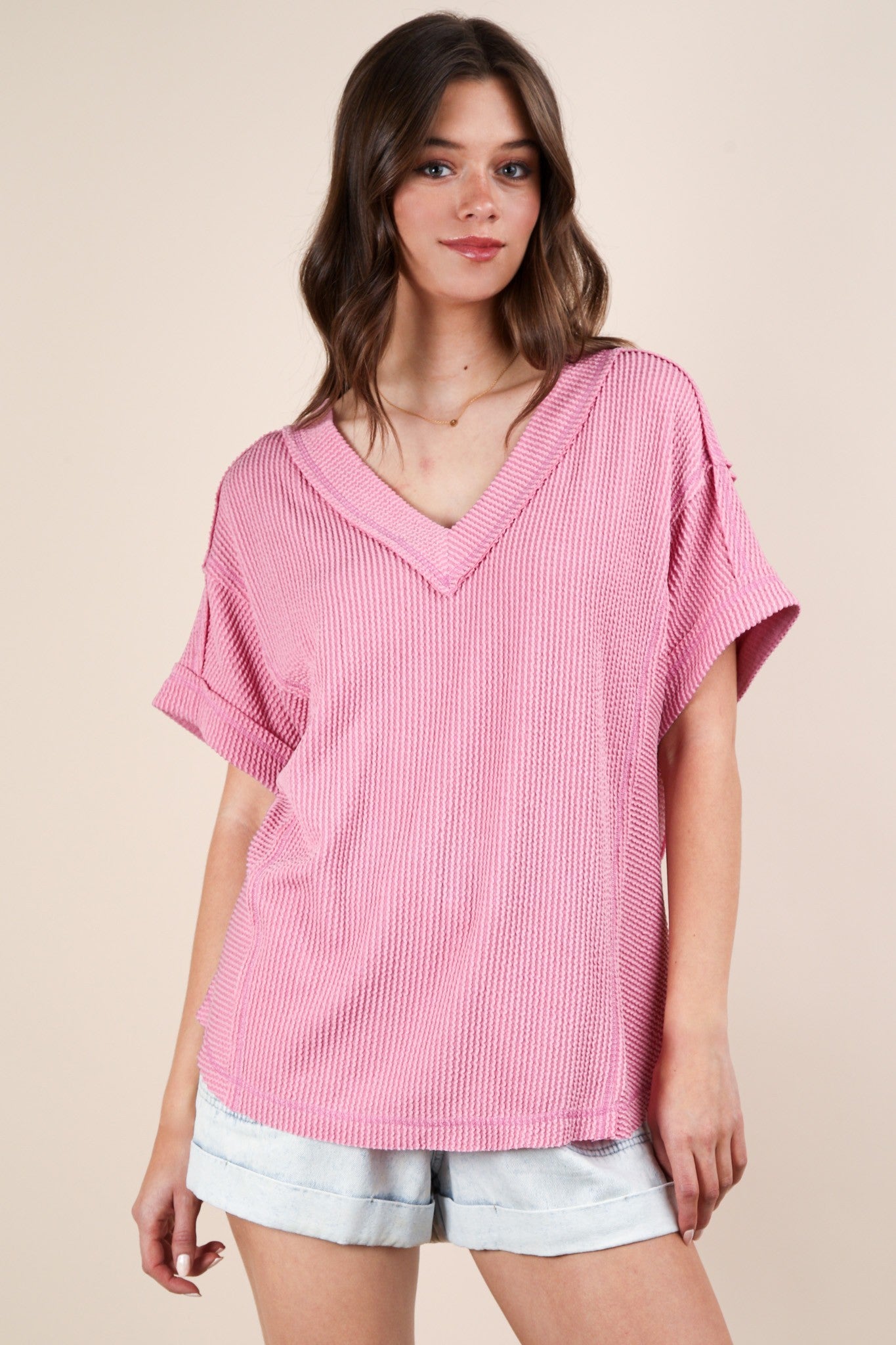 woman wearing a pink short sleeve v-neck top with a textured pattern and casual style, paired with light denim shorts