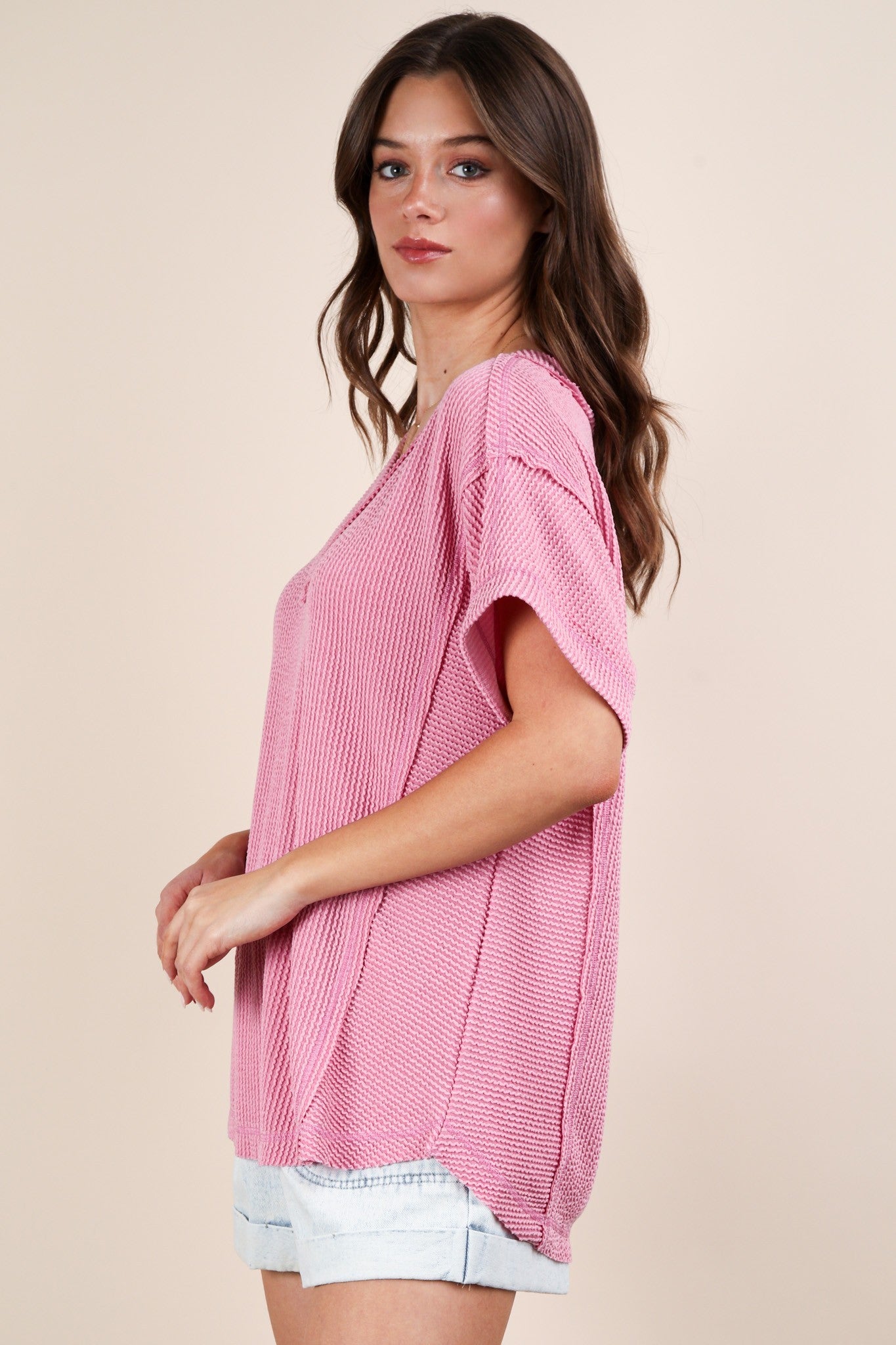 woman wearing a light pink short sleeve oversized sweater with a relaxed fit and side slits, paired with denim shorts
