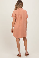 woman wearing a blush pink short sleeve maternity dress with a relaxed fit and back pleat detail.