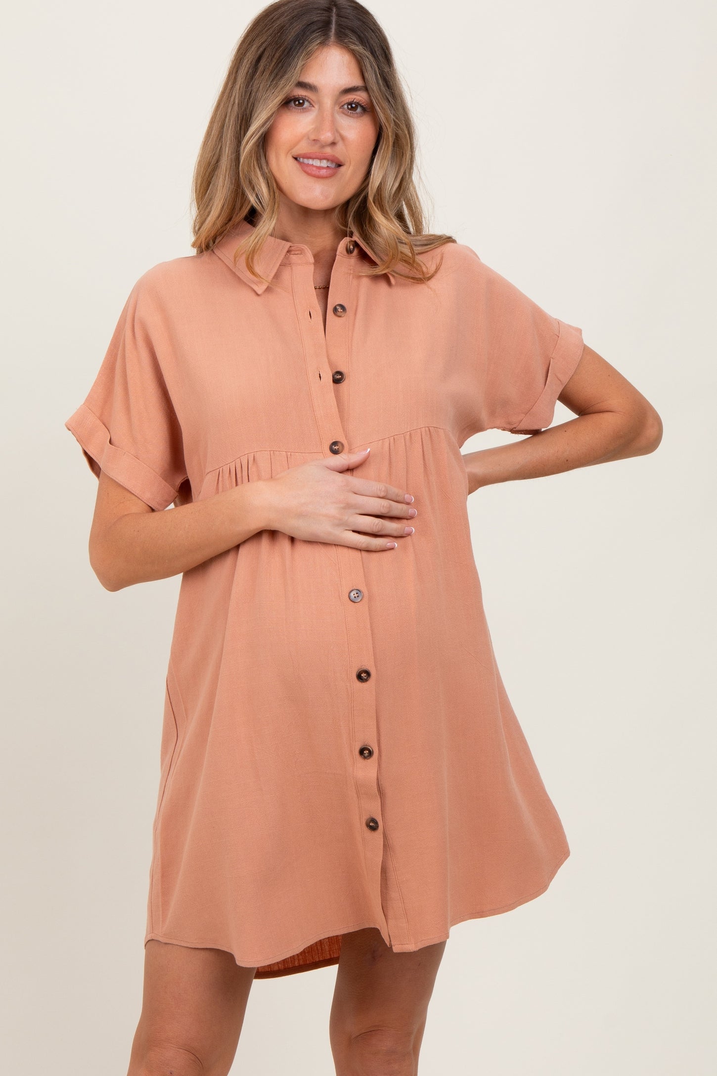woman wearing a rust-colored maternity button-up dress with short sleeves and a gathered waist, holding her baby bump