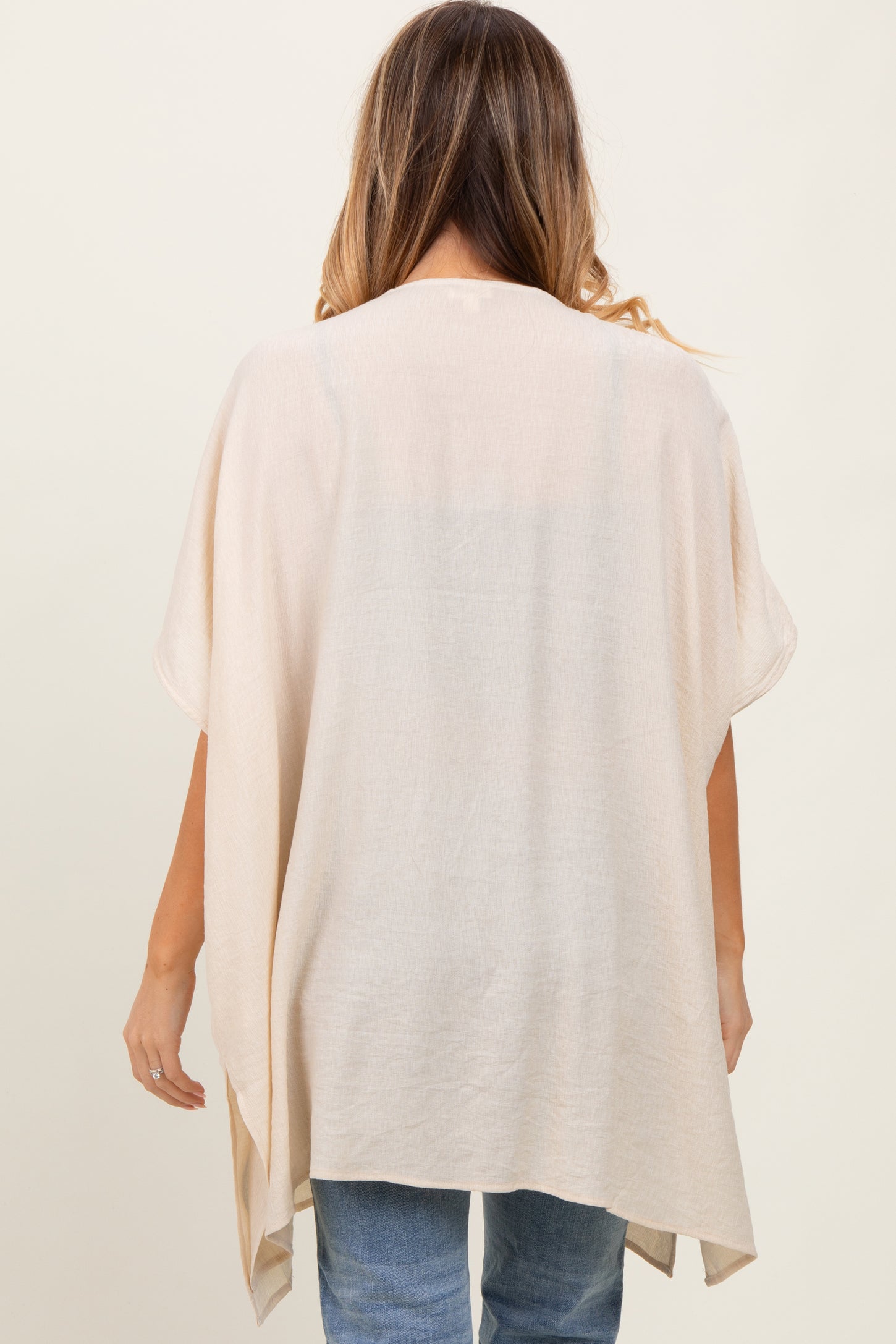 woman wearing a neutral beige open-front kimono style top with loose sleeves and a relaxed fit