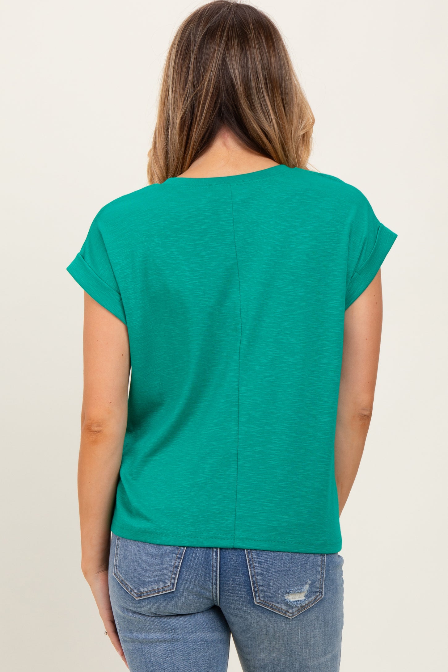 woman wearing a green short sleeve top with a relaxed fit and back seam detail, paired with blue jeans