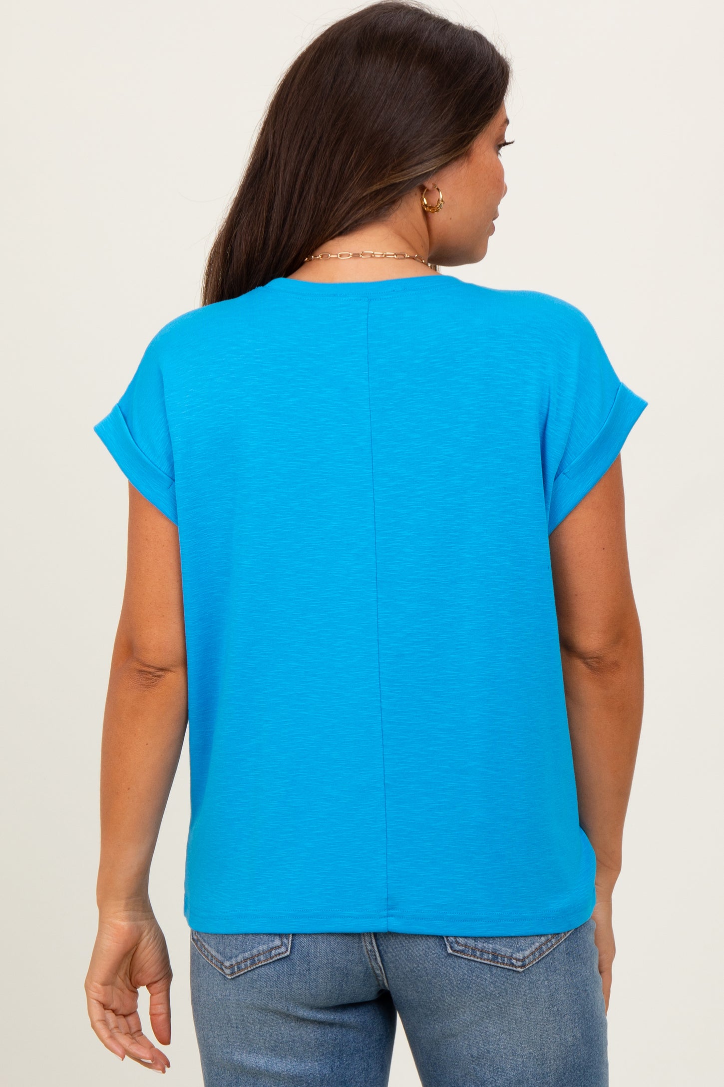 woman wearing a bright blue short sleeve maternity top, viewed from the back, paired with denim jeans