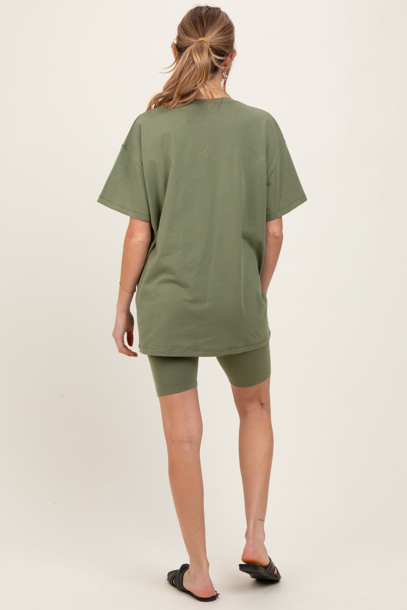 woman wearing an olive green oversized t-shirt with matching bike shorts, styled casually for maternity wear