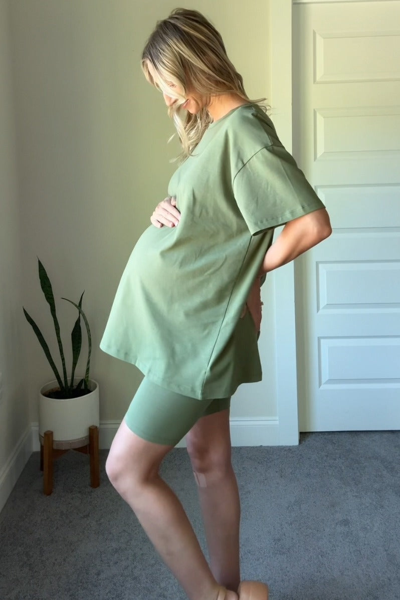 woman wearing a sage green maternity t-shirt and matching shorts, holding her baby bump