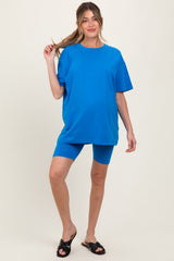 woman wearing a bright blue maternity oversized t-shirt and matching blue bike shorts, holding her hair up with one hand