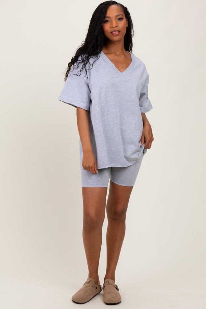 woman wearing a gray oversized v-neck t-shirt and matching bike shorts, standing against a neutral background