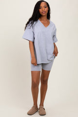 woman wearing a gray oversized v-neck t-shirt and matching bike shorts, standing against a neutral background