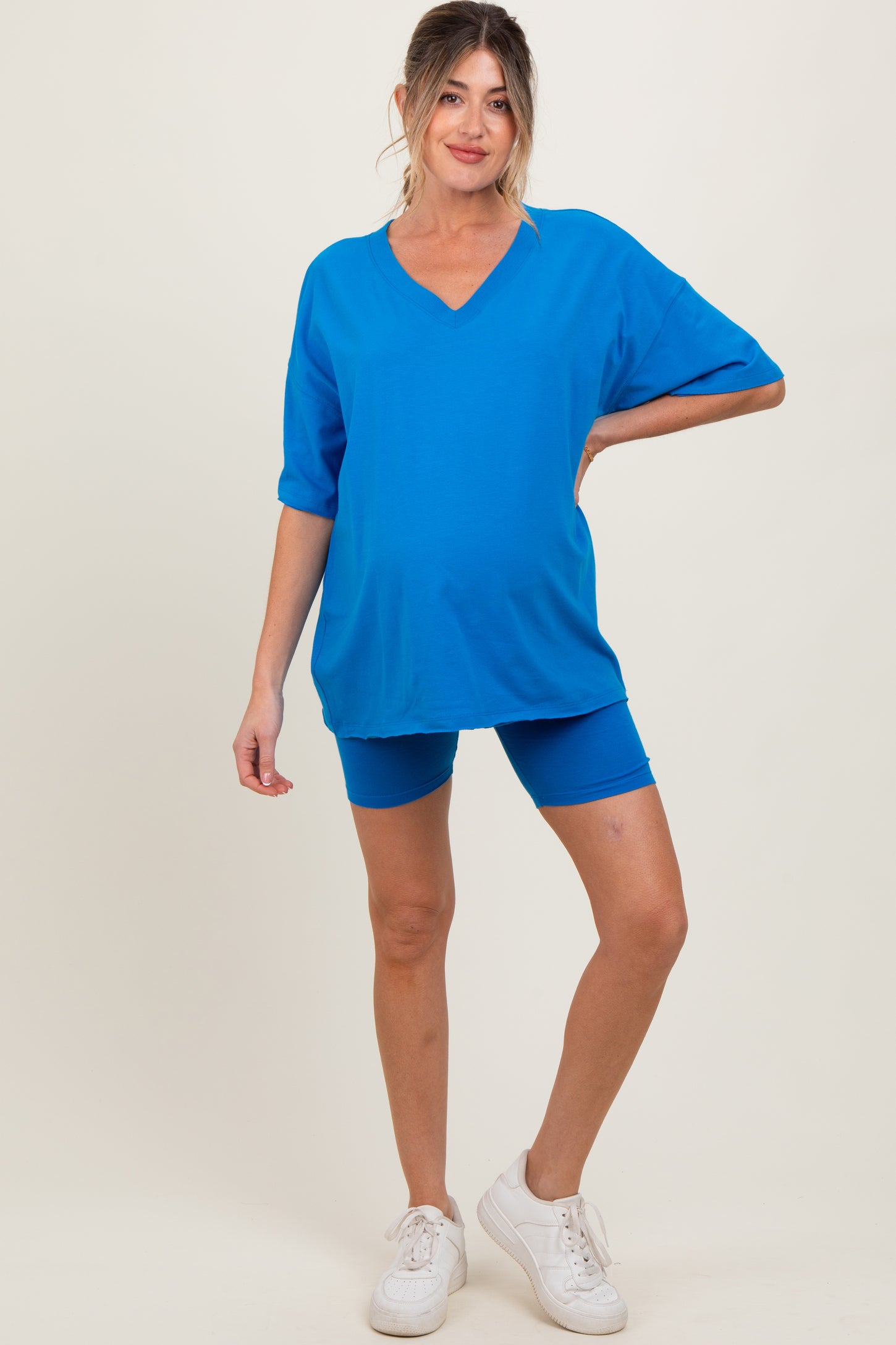 woman wearing a bright blue oversized maternity top and matching bike shorts, showcasing her baby bump
