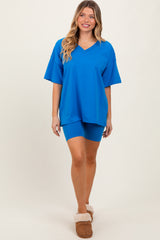 woman wearing a bright blue oversized v-neck t-shirt and matching bike shorts, styled with cozy slippers