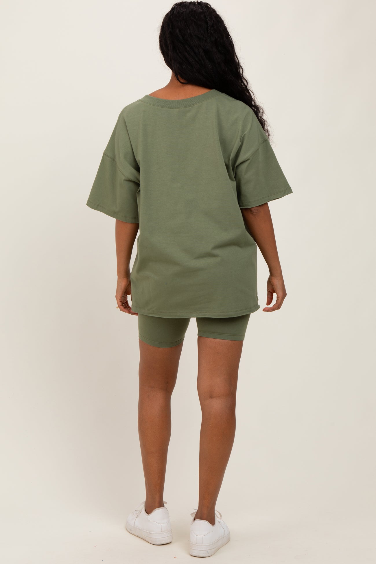 woman wearing an oversized olive green t-shirt and matching bike shorts, standing with her back to the camera