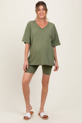 woman wearing an olive green oversized v-neck maternity tee and matching bike shorts, showing her baby bump