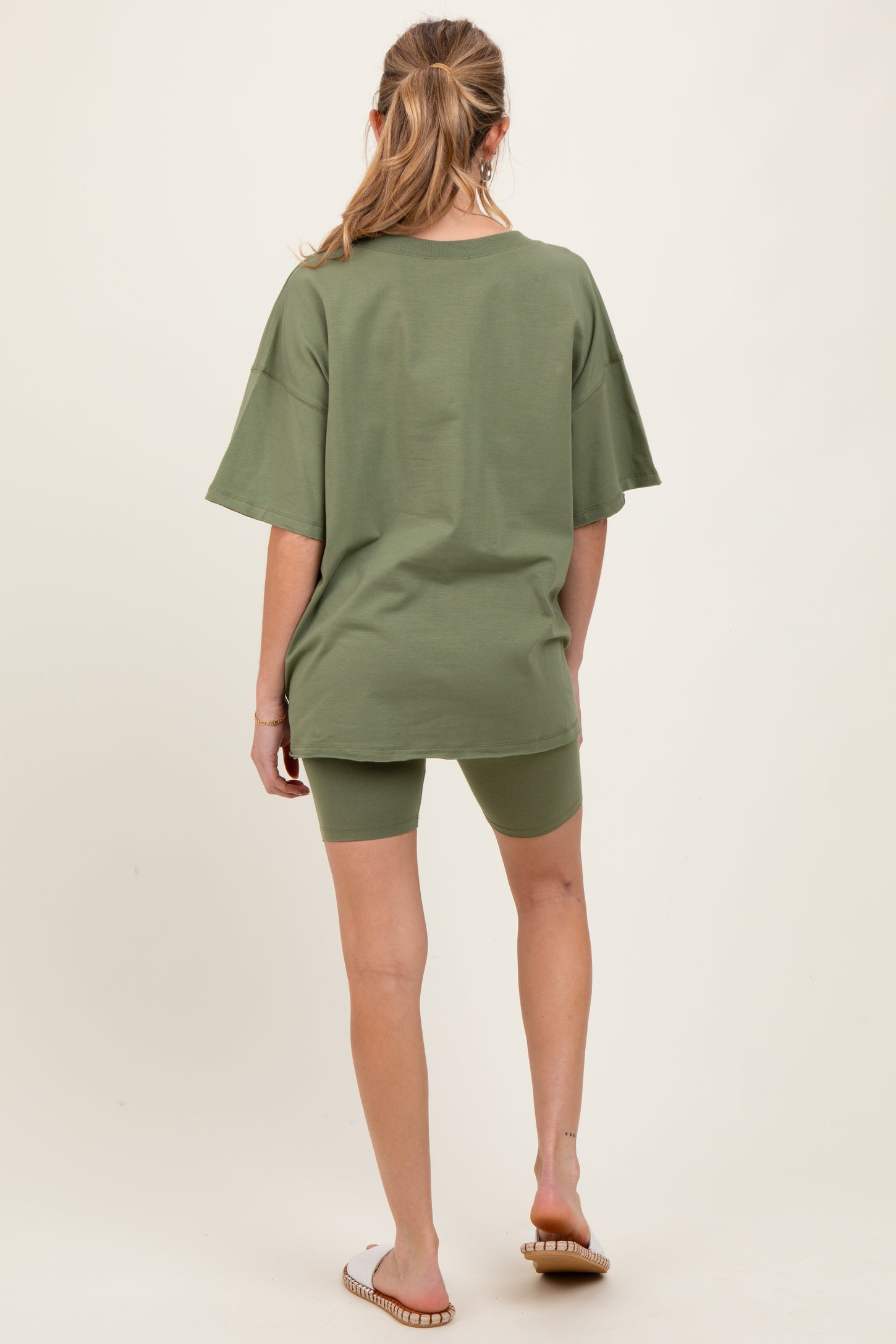 woman wearing an olive green oversized maternity t-shirt and matching bike shorts, showing a casual outfit from the back