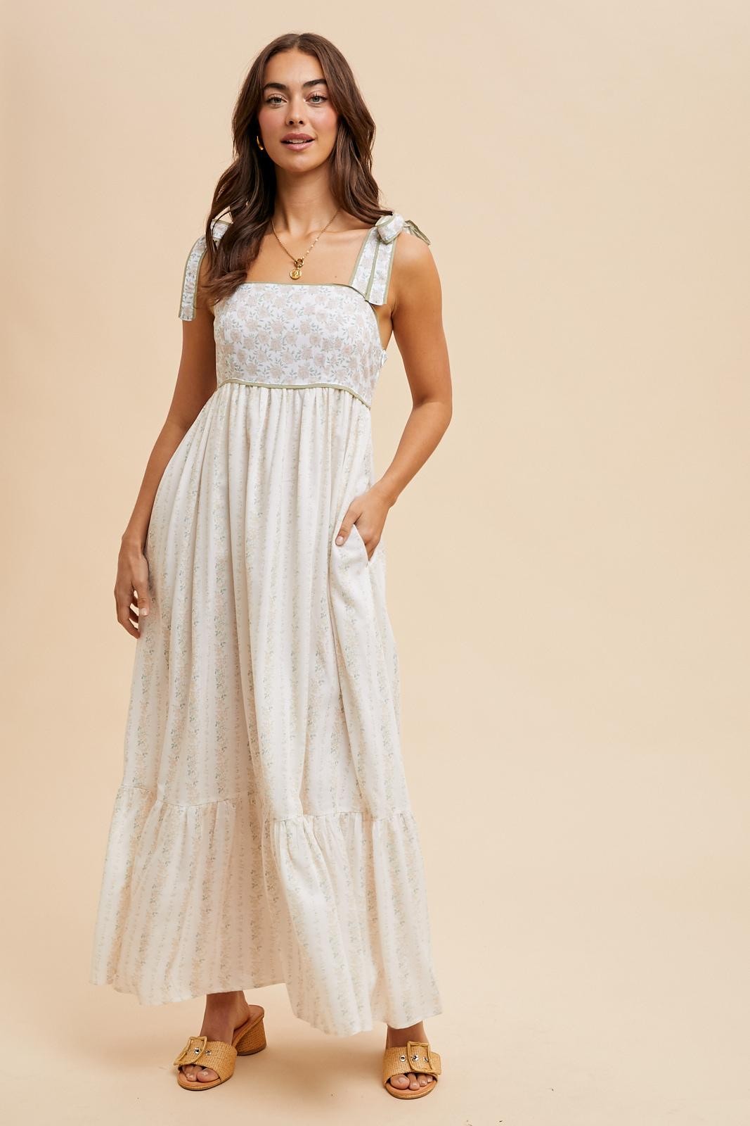 woman wearing a white floral print maxi dress with tiered skirt and tie straps, posing with one hand in pocket