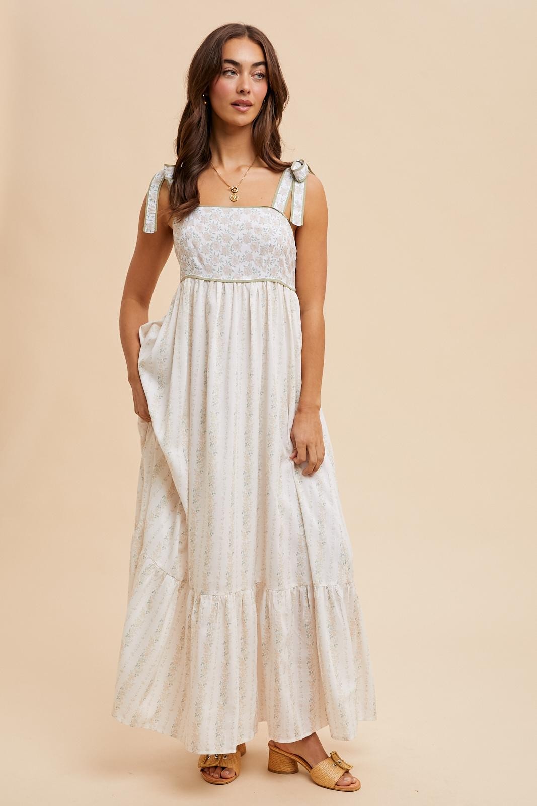 woman wearing a white floral maxi dress with ribbon straps and tiered skirt, standing against a neutral background